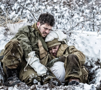 Pair of World War II soldiers huddled together in a shallow trench in a snow-covered landscape
